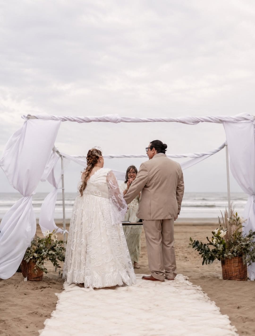 Novios dándose el sí bajo el altar de telas blancas, frente al mar